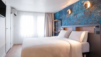 Ein Hotelzimmer mit einem großen Bett, einem Spiegel, einer Wandleuchte und einem Fenster mit Vorhängen.