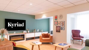 A modern living room with a television, sofas, a fireplace, and artwork on the walls. - Hotel Kyriad Argenteuil (Argenteuil)