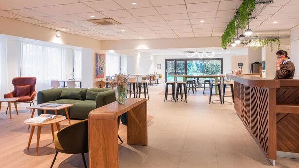 A modern interior with a reception desk, seating area, and large windows. - Hotel Kyriad Argenteuil (Argenteuil)