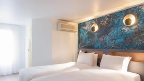 A hotel room with a large bed, a wall-mounted air conditioner, and a textured blue wall. - Hotel Kyriad Argenteuil (Argenteuil)