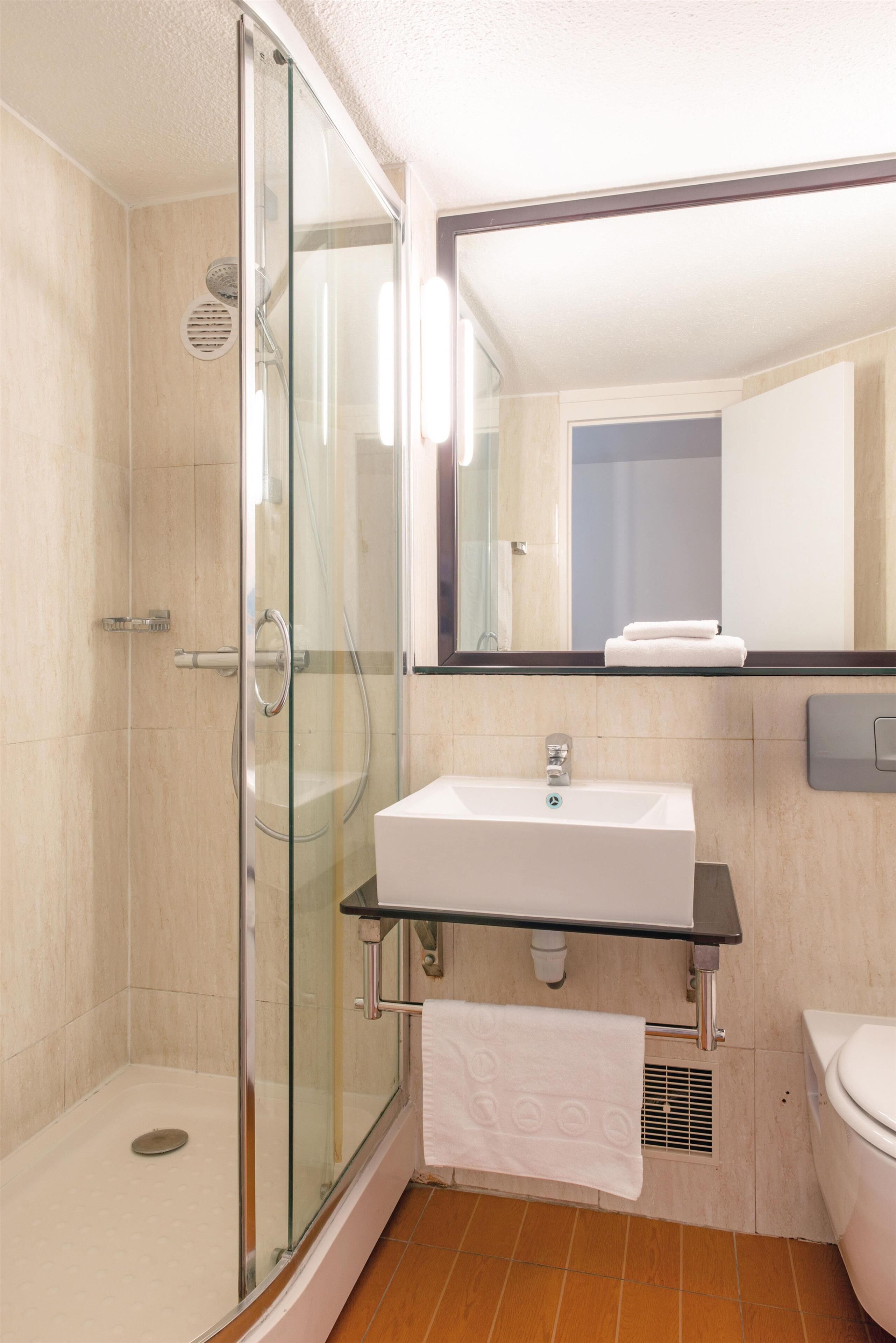 Un baño moderno con cabina de ducha de vidrio, un lavamanos blanco y un espejo sobre él.