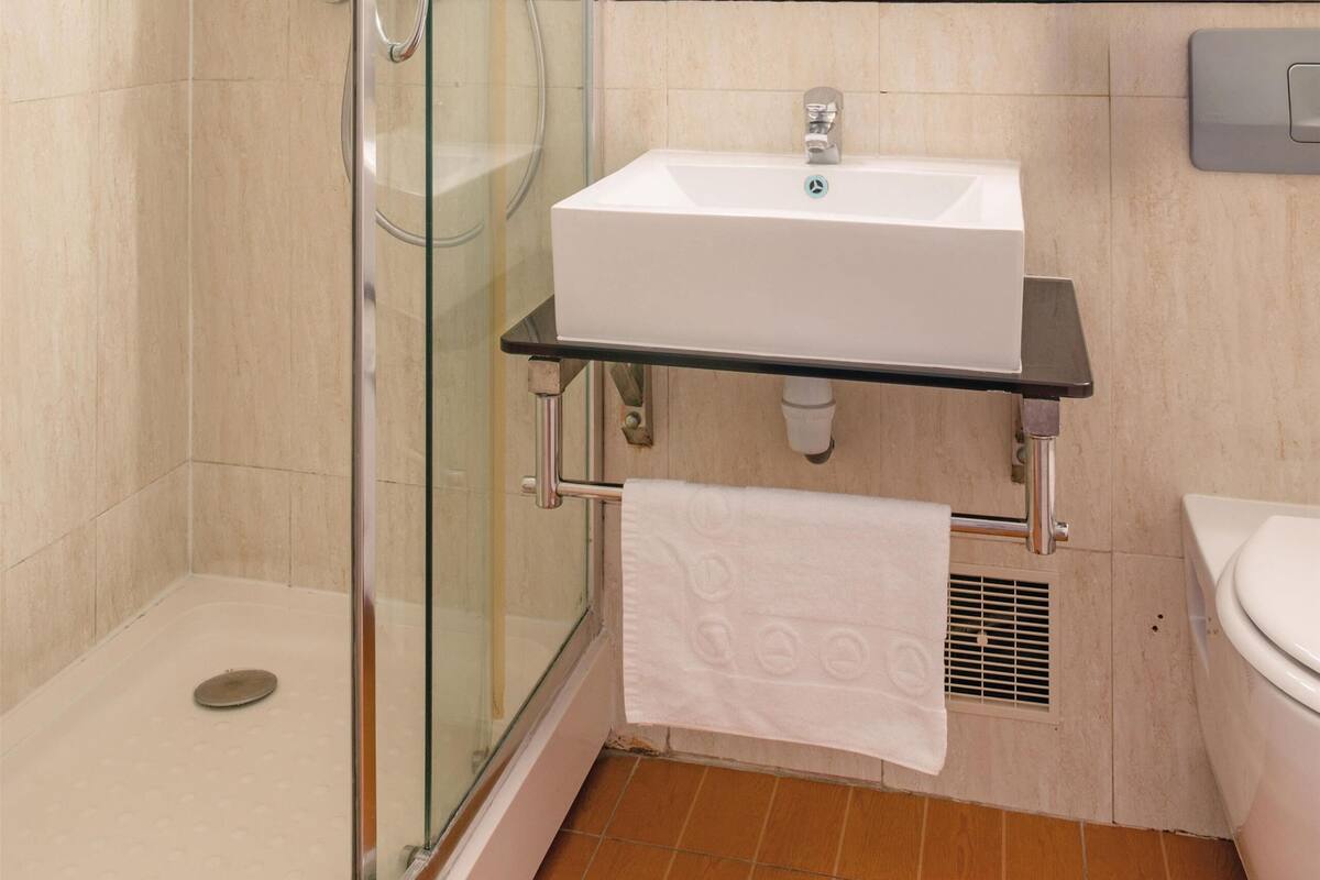 Un baño moderno con cabina de ducha de vidrio, un lavamanos blanco y un espejo sobre él.