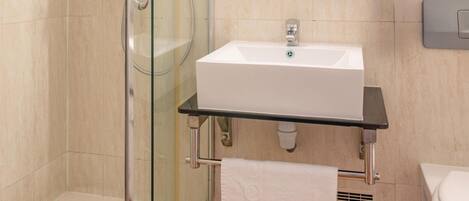 Un baño moderno con cabina de ducha de vidrio, un lavamanos blanco y un espejo sobre él.