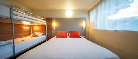 Ein Hotelzimmer mit Etagenbett, einem Einzelbett und einem großen Fenster.