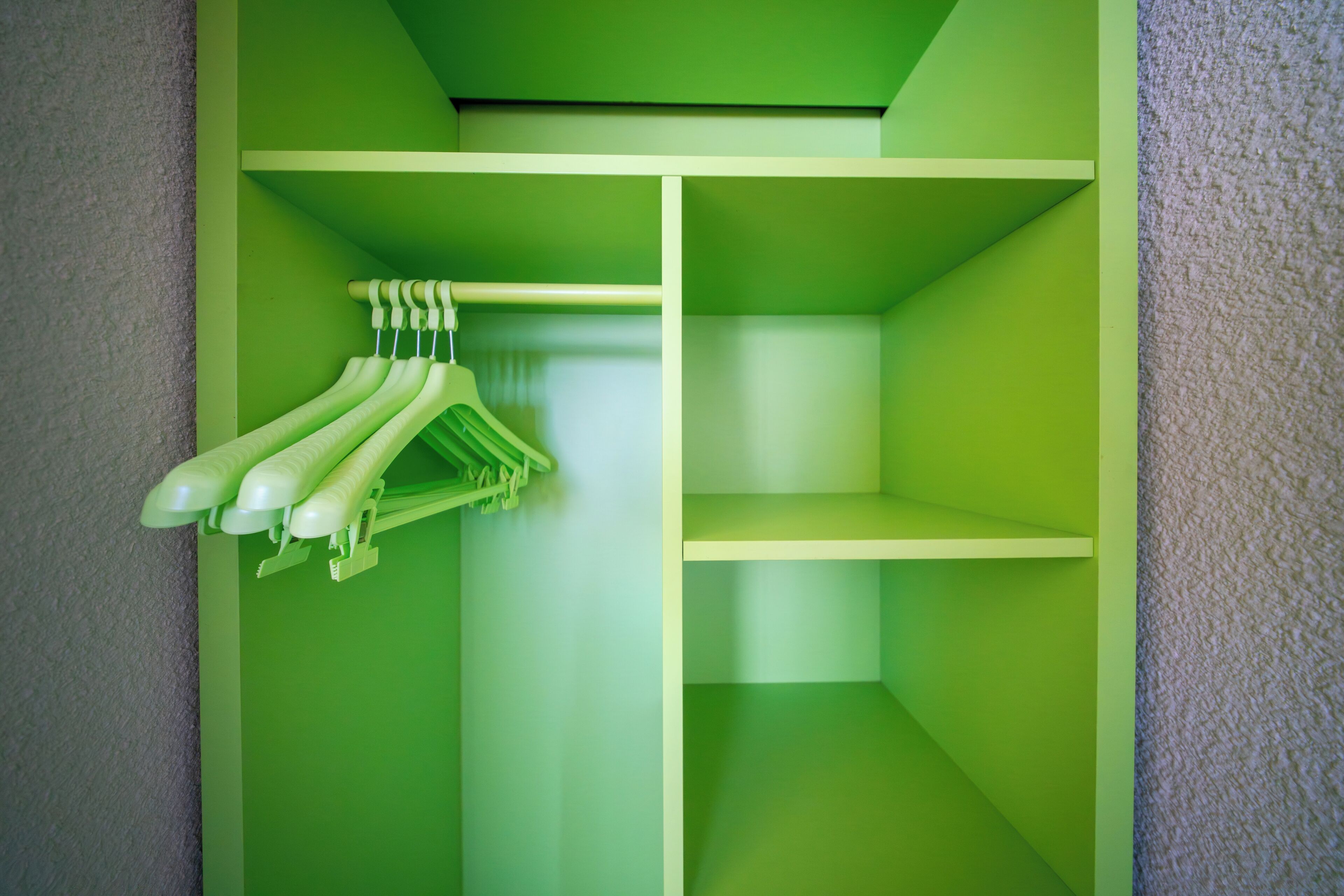 A green closet with hanging space for clothes and shelves.
