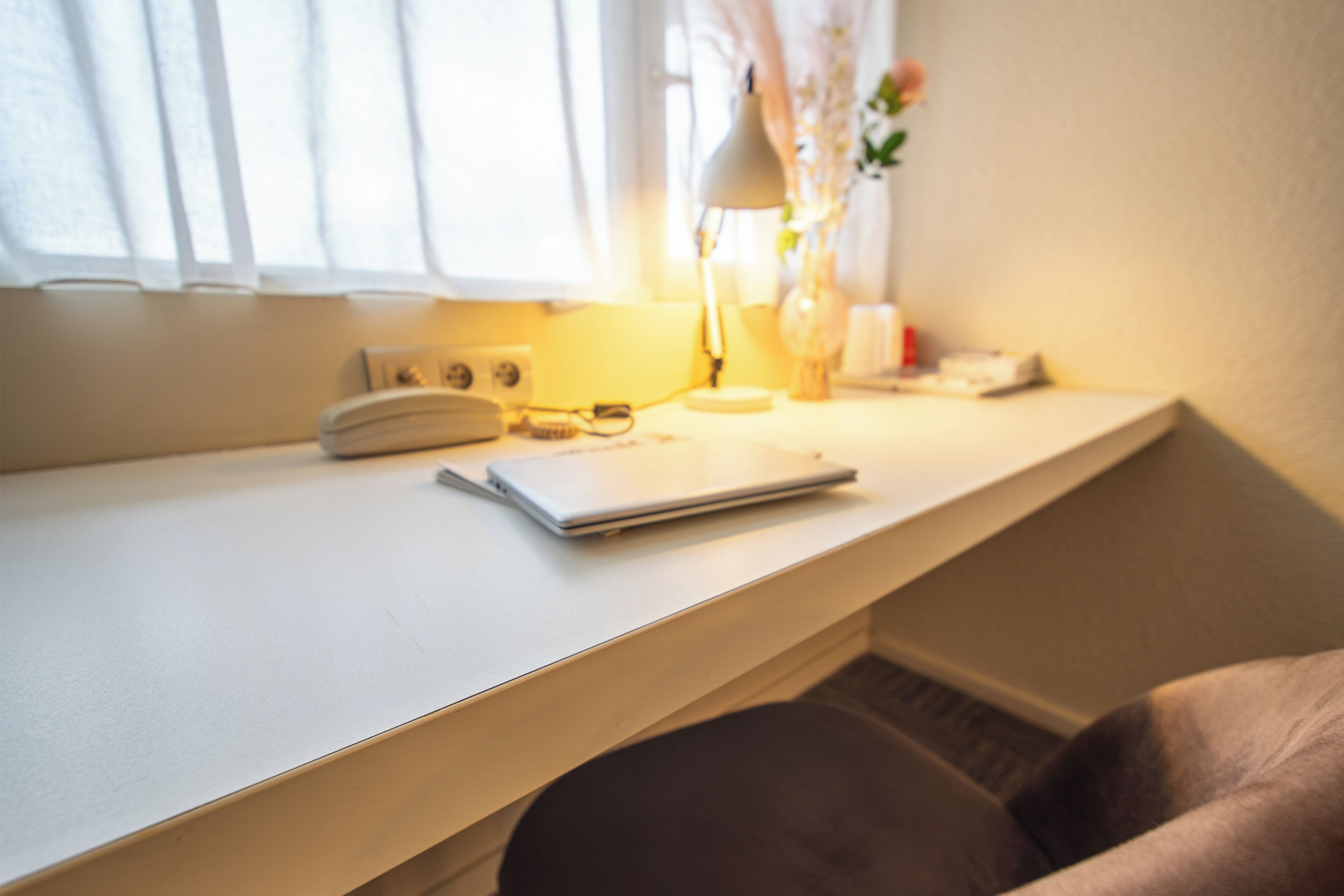 A corner of a room with a desk, a lamp, a laptop, and a chair.
