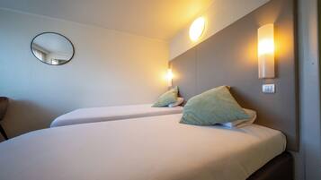 Una camera d'albergo con due letti, uno specchio rotondo e luci a parete.