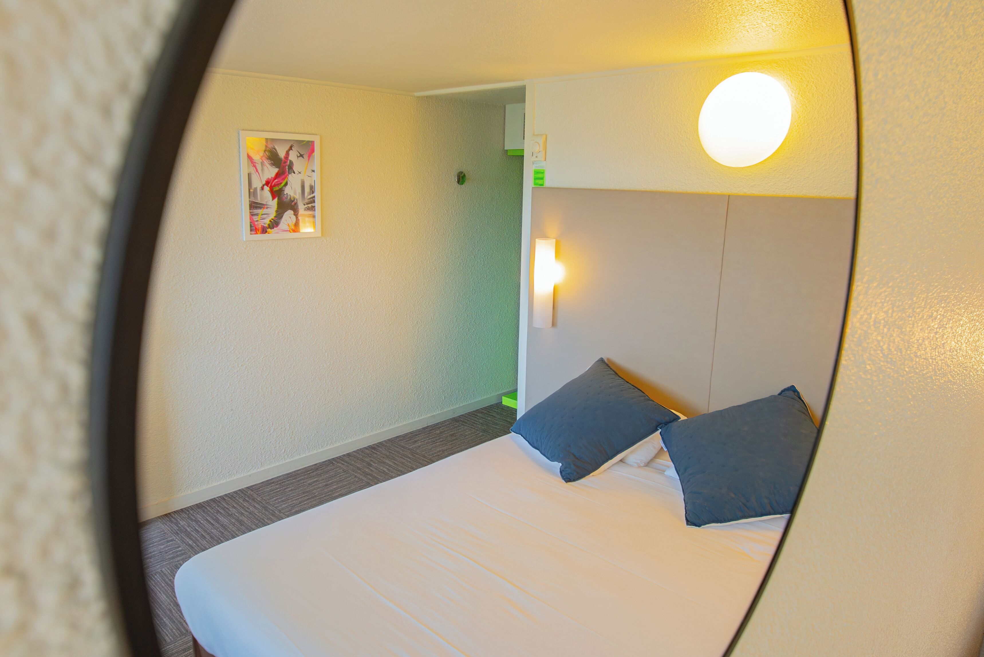 Ein Hotelzimmer mit einem Bett, zwei Kissen, einer Wandleuchte und einer Tür.
