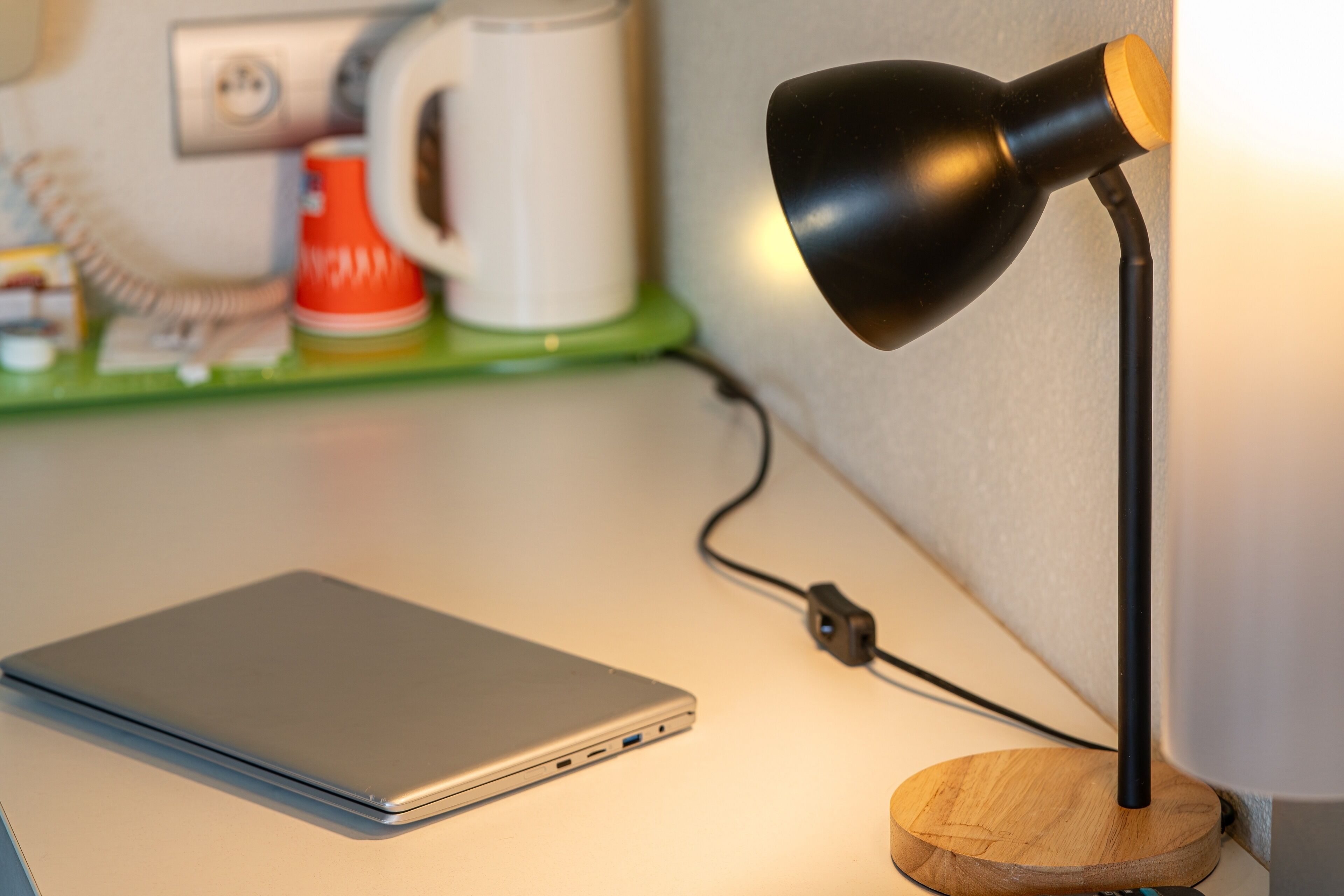 A laptop on a desk with a desk lamp and a power cord.