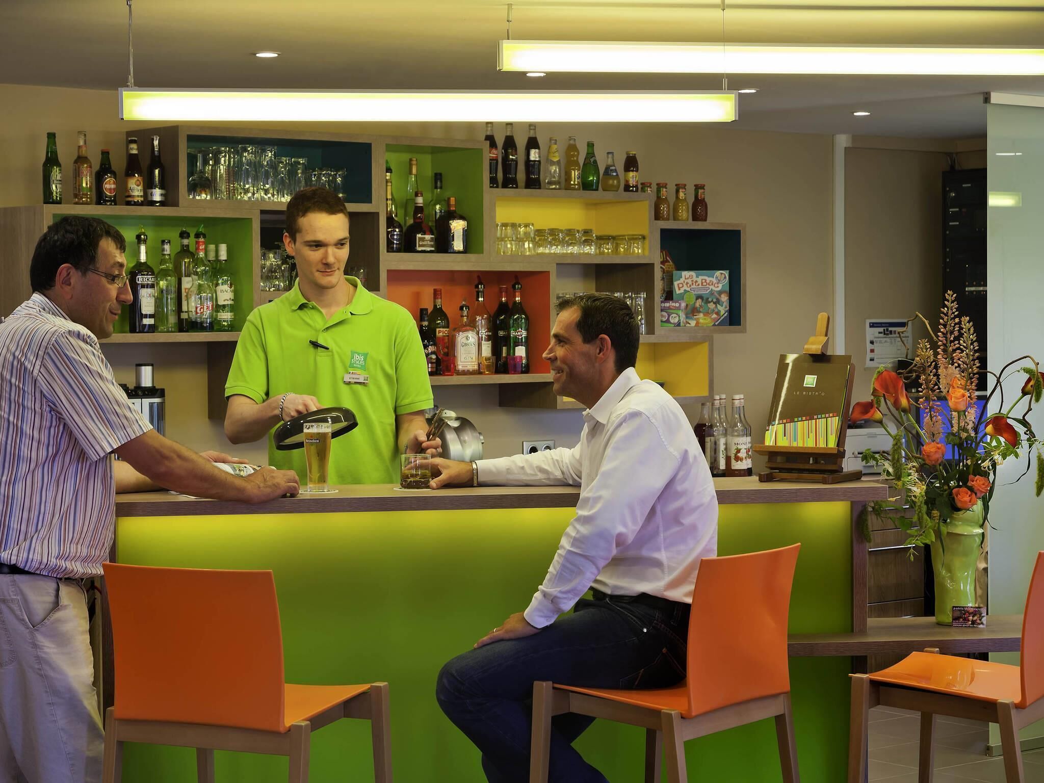 Een bar met een bartender, een klant en een toonbank met verschillende flessen en glazen.