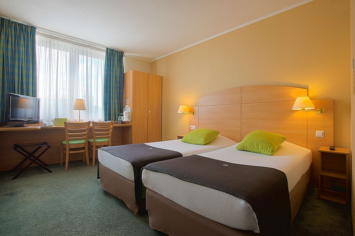A hotel room with two beds, a desk, chairs, and a television.