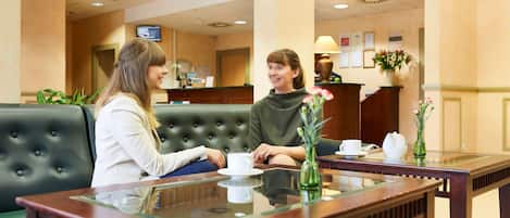 A reception area with a reception desk, a green upholstered sofa, and a glass-top table with a vase of flowers.