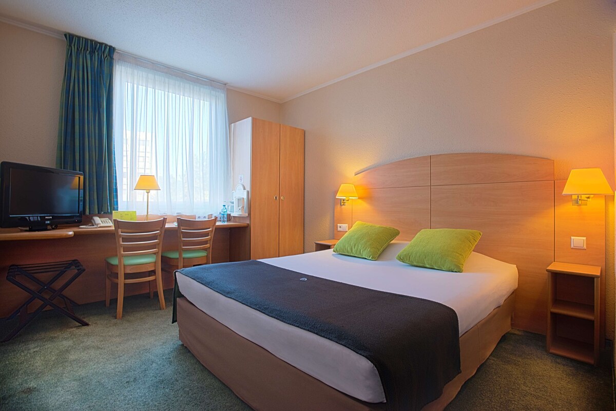 A hotel room with a bed, desk, chairs, and a television.