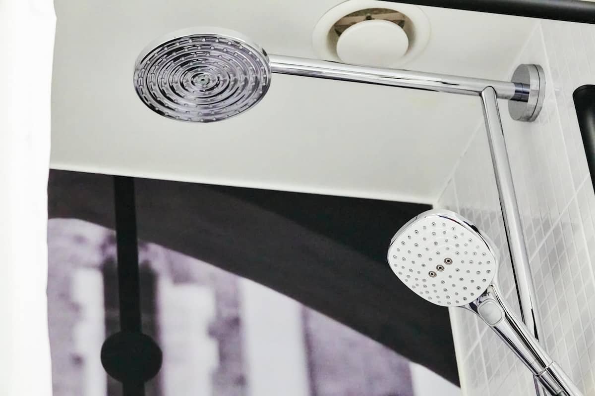 A shower with a handheld showerhead and a fixed showerhead mounted on a chrome bar.
