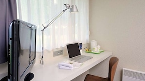 Habitación de hotel con escritorio, laptop, monitor, lámpara, silla y radiador.