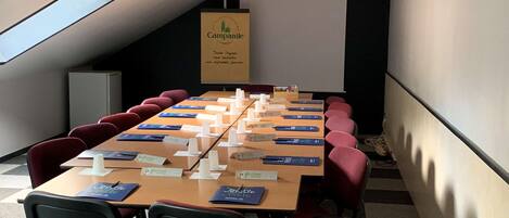 Een vergaderzaal met een lange tafel, rode stoelen, naamkaartjes en een scherm voor een beamer.