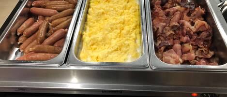 Un bufé con tres opciones de comida: salchichas, huevos revueltos y tocino.
