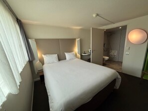 Une chambre d’hôtel avec un grand lit, des tables de chevet, une commode, une salle de bain avec des toilettes et un lavabo, et un espace douche.