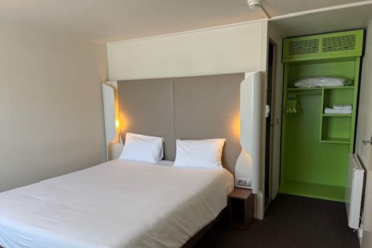 Une chambre d’hôtel avec un lit, des tables de chevet, une armoire verte et un radiateur blanc.
