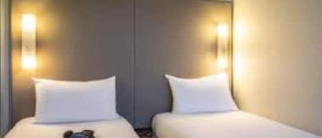 Una camera d'albergo con due letti, ciascuno con biancheria da letto bianca e un cuscino. Su ciascun lato dei letti sono presenti due luci a parete.