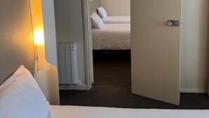 Una habitación de hotel con una cama, una lámpara de noche, un radiador y una puerta que da a otra habitación.