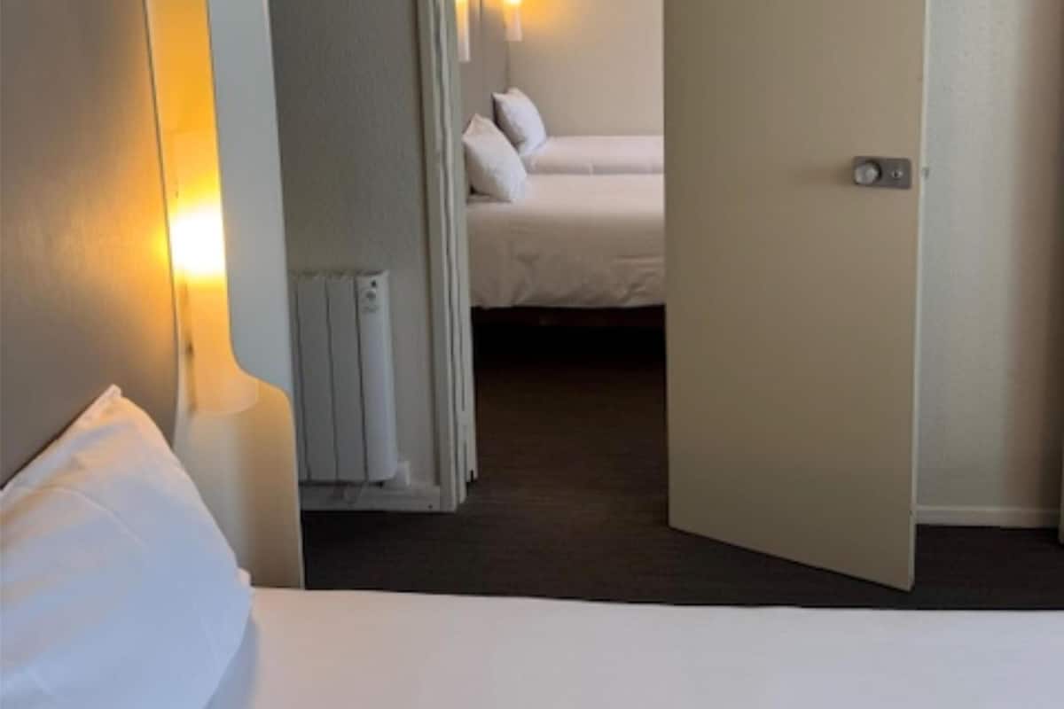 Une chambre d’hôtel avec un lit, une lampe de chevet, un radiateur et une porte donnant sur une autre pièce.