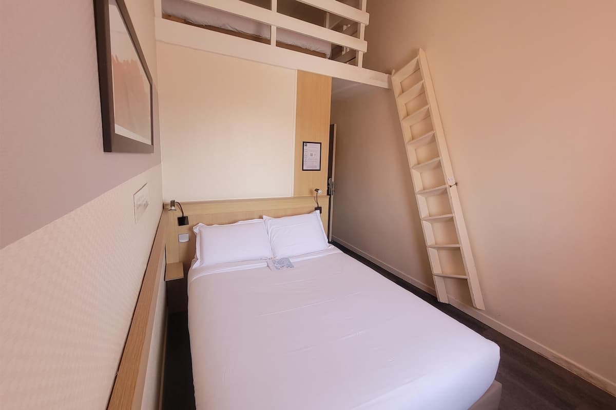 Quarto com cama, cabeceira, prateleira na parede e escada.