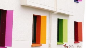 Un edificio de varios pisos con paredes blancas y contraventanas de colores.