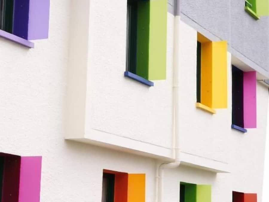 Un immeuble à plusieurs étages avec des murs blancs et des volets colorés.