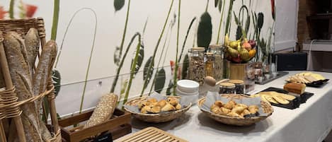 Una mesa con diversos panes y pasteles, incluyendo baguettes y croissants, sobre un mantel con un fondo floral.