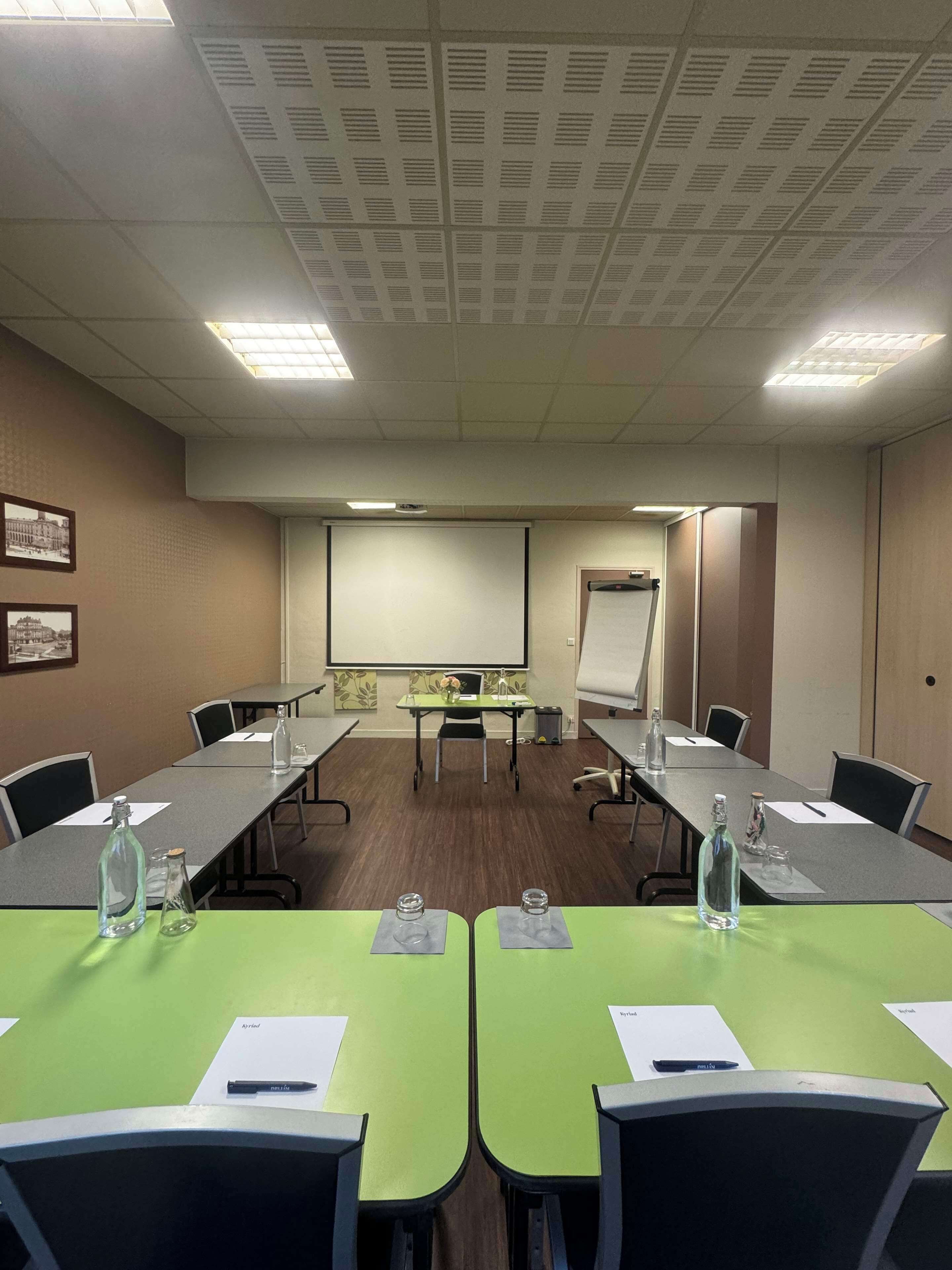 A conference room with a long table, chairs, a projector screen, and a whiteboard.