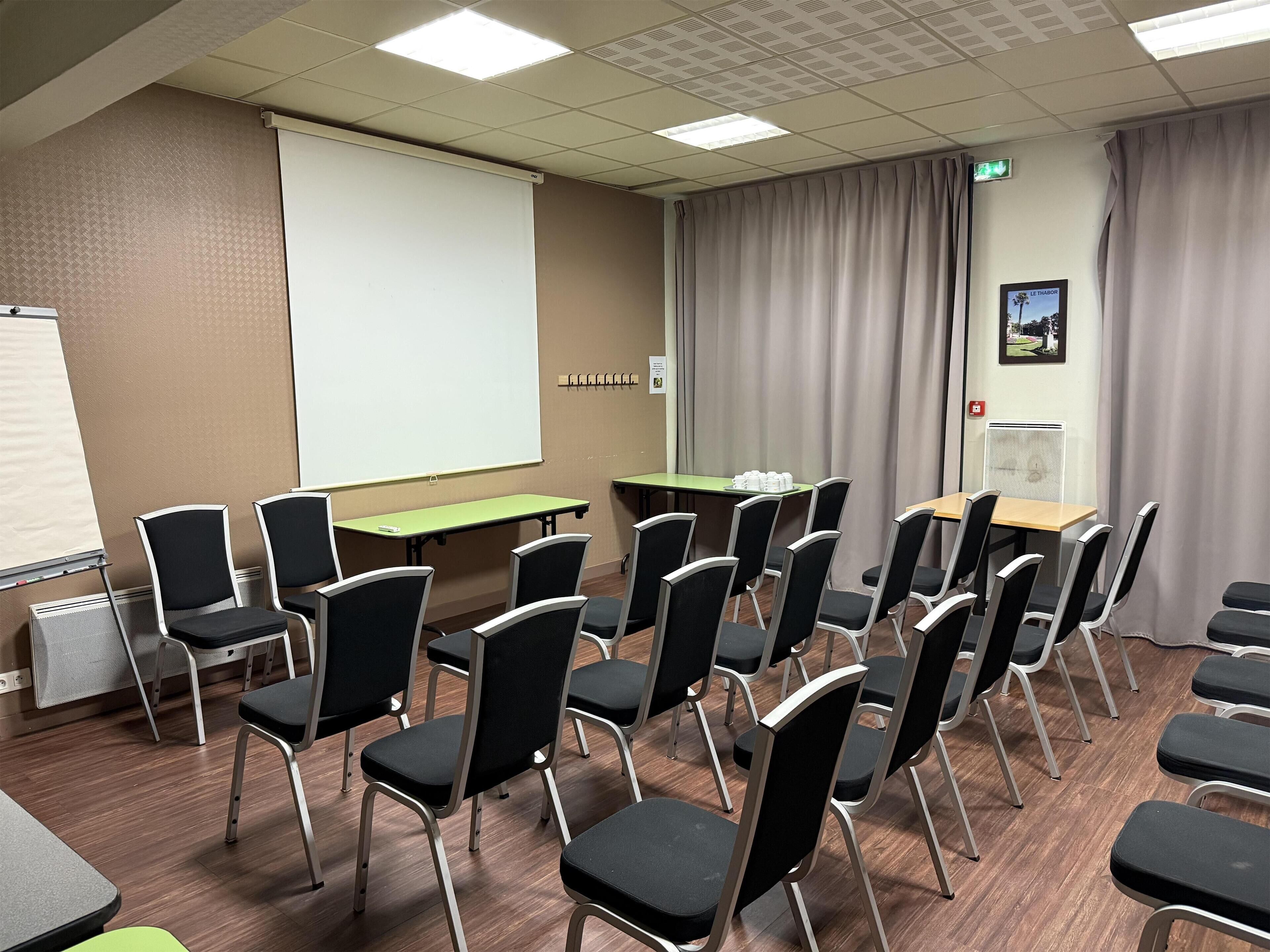 A conference room with a projector screen, tables, chairs, and a picture on the wall.