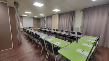 Sala de conferência com mesas compridas, cadeiras e tela de projeção.