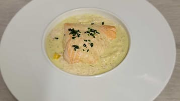 En hvid tallerken med en laksespfilet oven på cremet sauce, pyntet med purløg.