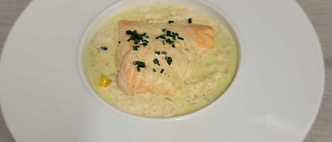 A white plate with a salmon fillet on a bed of creamy sauce, garnished with chives.