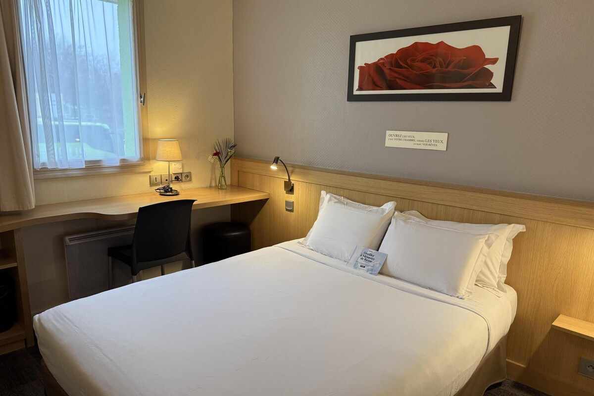 Habitación de hotel con cama, escritorio, silla, lámpara y un cuadro en la pared.