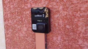 Un dispositivo fijado a la pared con una etiqueta negra que dice "wallbox" y "Badgés ici" sobre un muro rosa con textura.