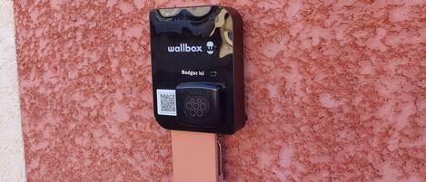 Un dispositivo fijado a la pared con una etiqueta negra que dice "wallbox" y "Badgés ici" sobre un muro rosa con textura.