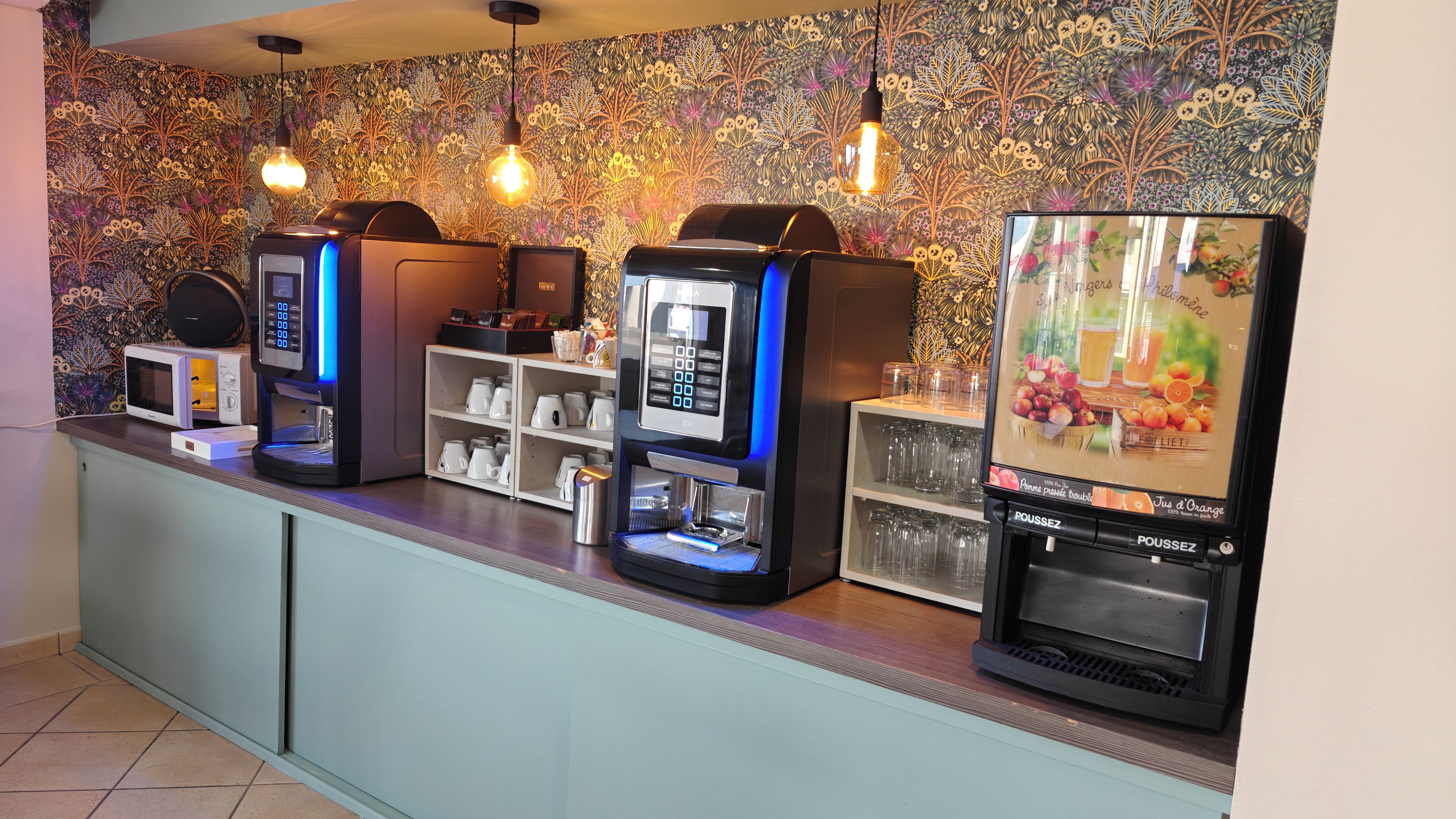 Una estación de bebidas de autoservicio con varias máquinas de café y un dispensador de zumo de frutas.
