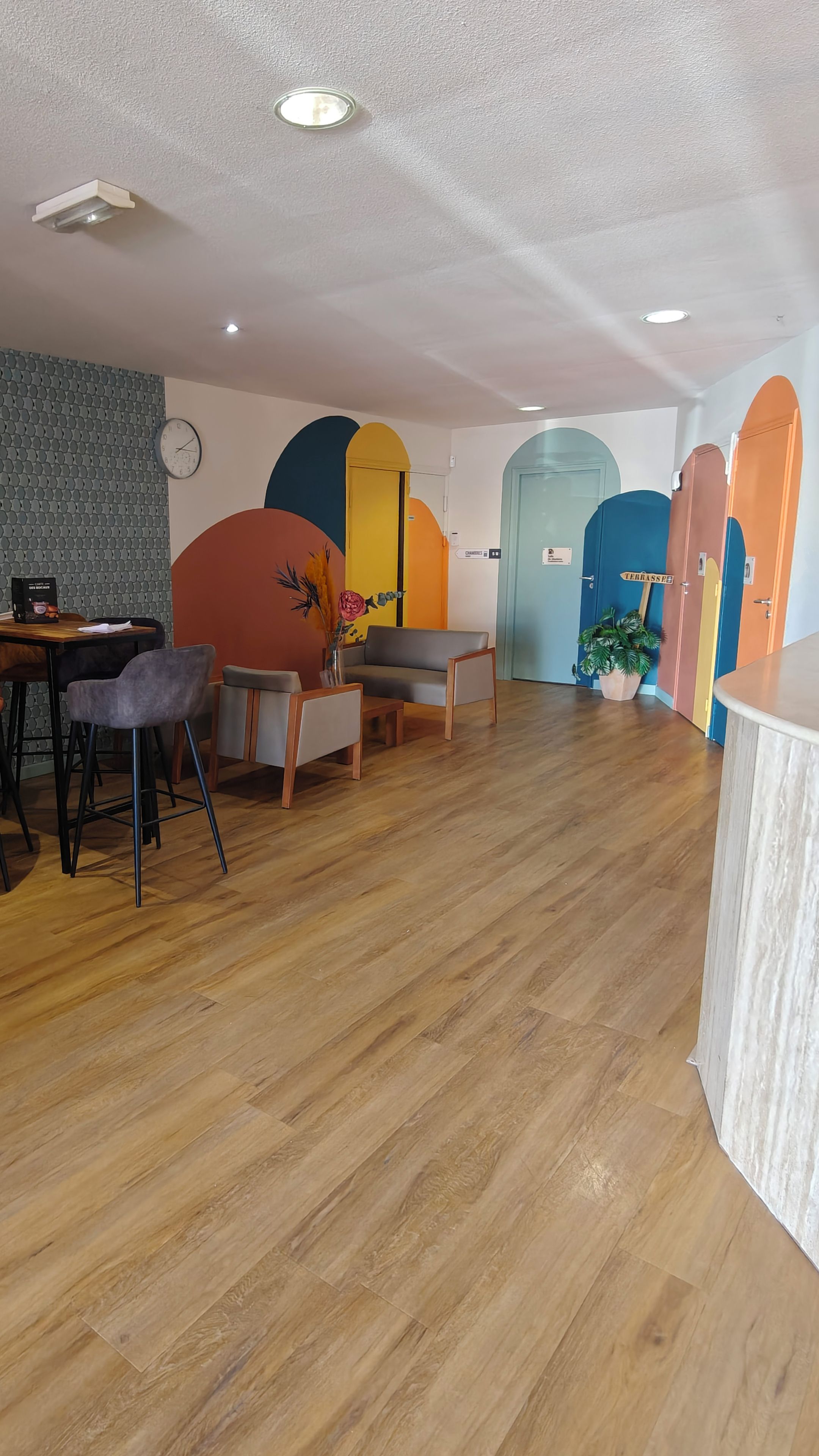Ein geräumiges Zimmer mit Holzboden, einer Couch, einem Esstisch mit Stühlen und farbenfrohen Wanddekorationen.