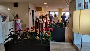 A hotel lobby with a reception desk, potted plants, and a large window. - The Originals City Hotel Hippocampe Sète Balaruc (Balaruc-le-Vieux)