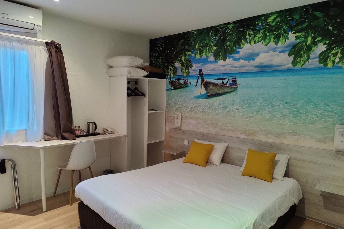 A bedroom with a bed, a desk, and a mural of a beach scene.