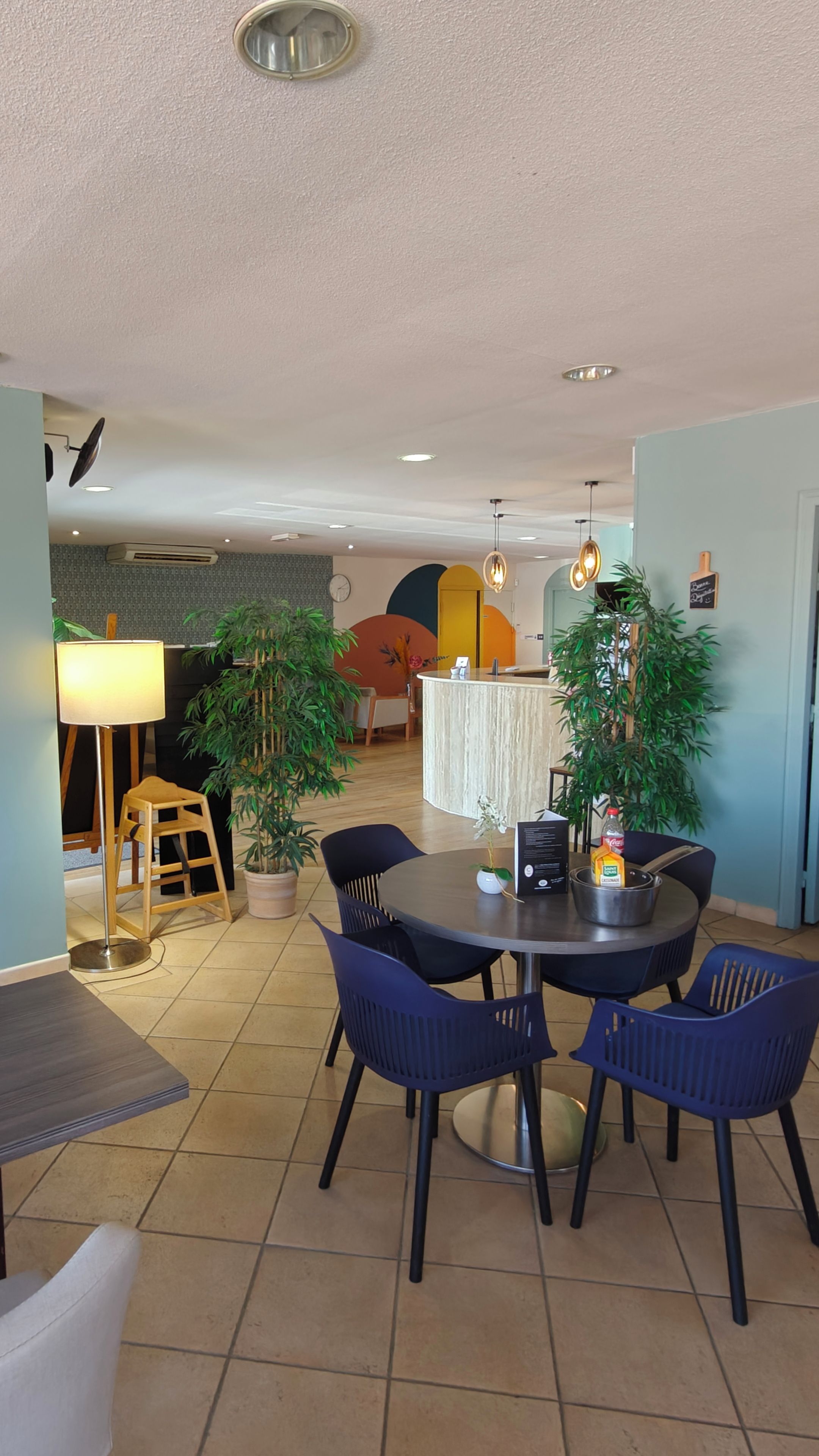 A dining area with a round table, chairs, and a lamp. There is a plant and a bottle on the table.