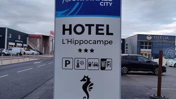 Un cartel anuncia The Originals City Hotel en L'Hippocampe, con estacionamiento, WiFi y el logotipo de un caballito de mar.