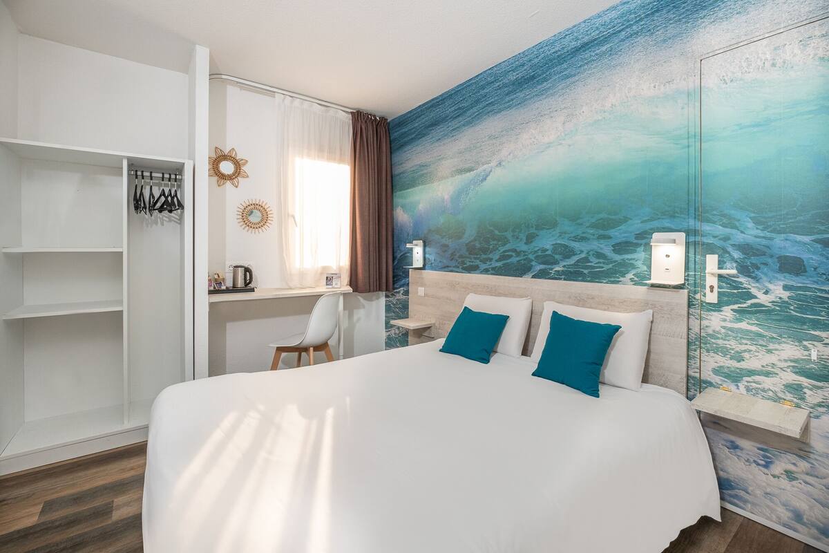 A hotel room with a bed, a desk, and a wardrobe.