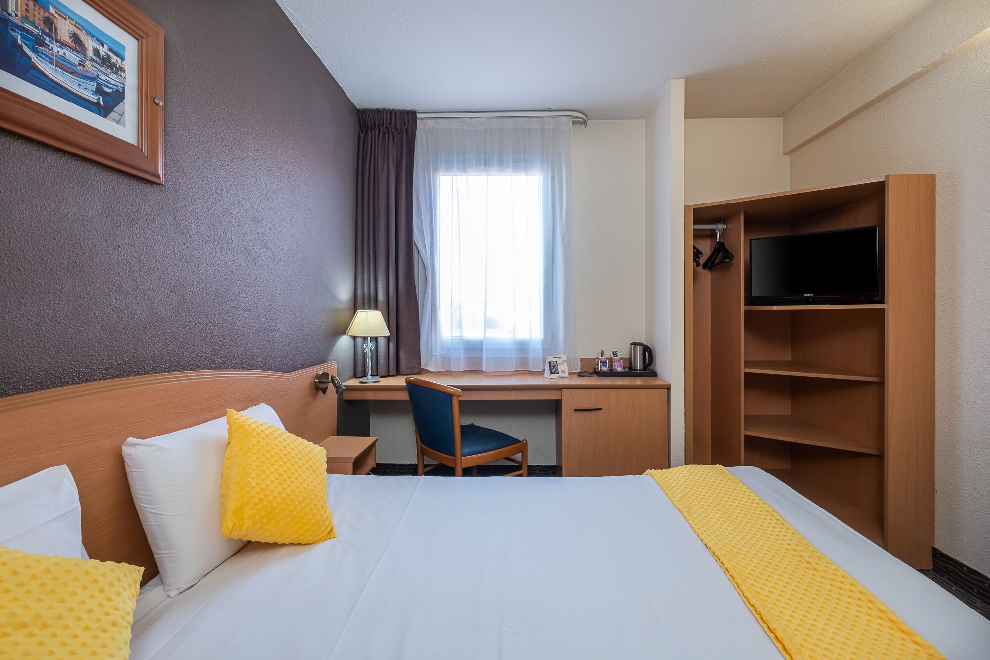 Habitación de hotel con cama, escritorio, silla, televisor y armario.