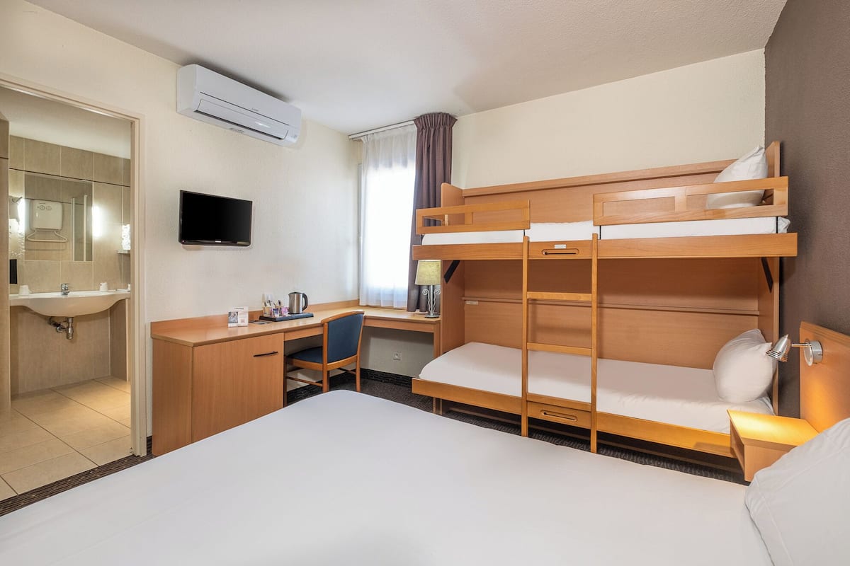 A hotel room with a bunk bed, a desk with a chair, a sink, a mirror, and a flat-screen TV.