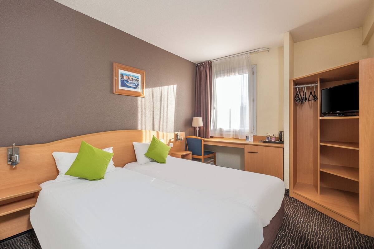 A hotel room with a large bed, a desk, a television, and a wardrobe.