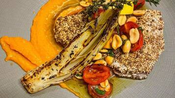 Un plato con pescado a la parrilla, espárragos, tomates cherry y salsa cremosa.