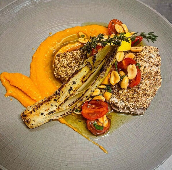 A plate with grilled fish, asparagus, cherry tomatoes, and a creamy sauce.
